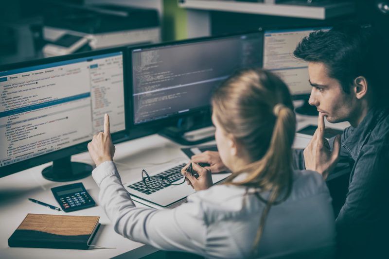 Simplifying software: Two developers working together behind mutiple monitors